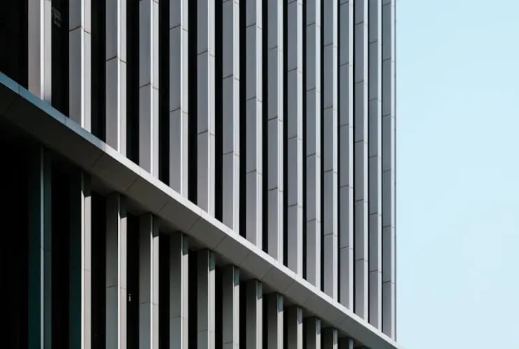 Modern office building facade with vertical metal louvers and glass windows against light blue sky