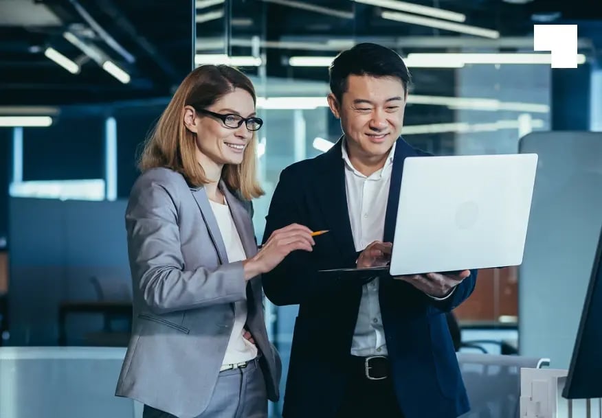 Two business professionals collaborating on operational risk management solution using laptop in modern office
